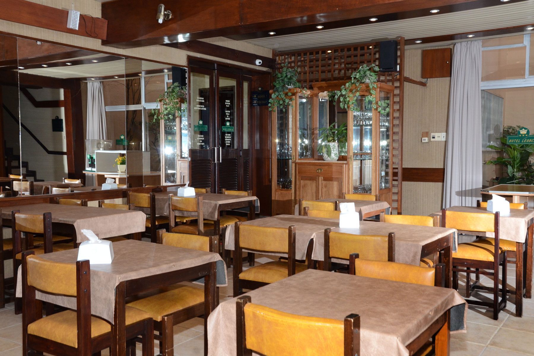 Comedor del hotel con mesas de madera, sillas tapizadas en cuero ocre y espejos
