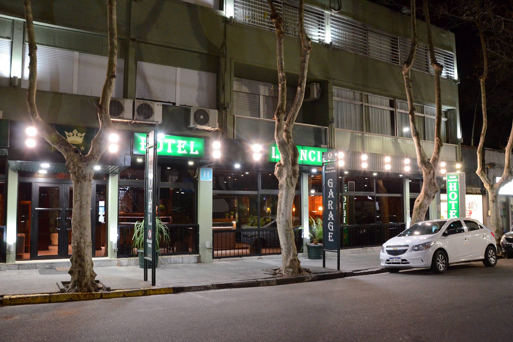 Fachada del Hotel Leoncia de noche, con el cartel verde iluminado bajo los plátanos de la calle Rivera