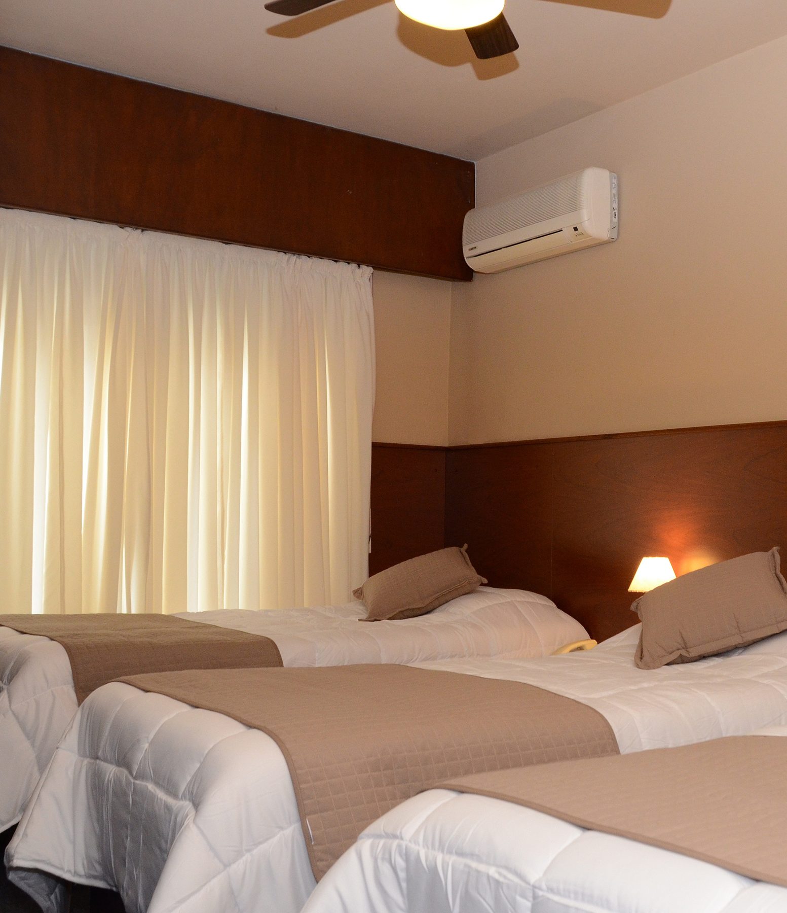 Habitación triple con tres camas individuales, pies de cama beige y ventilador de techo